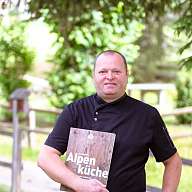 Mann in schwarzer Kochjacke und Buch in der Hand